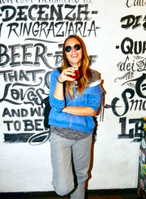 A person stands in front of a black-and-white word mural at Artisan, a trendy bar, drink in hand.