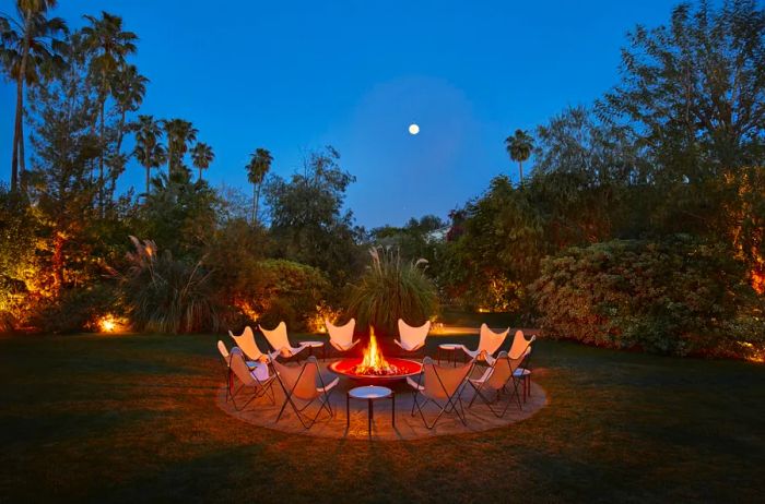 Ten vacant white butterfly chairs are arranged around a firepit under a starry night sky, surrounded by palm trees and a full moon.