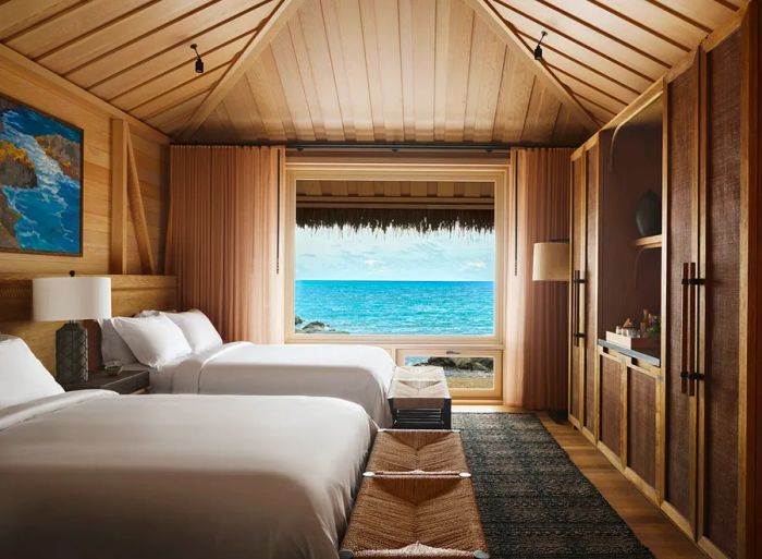 A guest room featuring two beds, soaring ceilings, wooden floors, and stunning views of the Pacific Ocean.