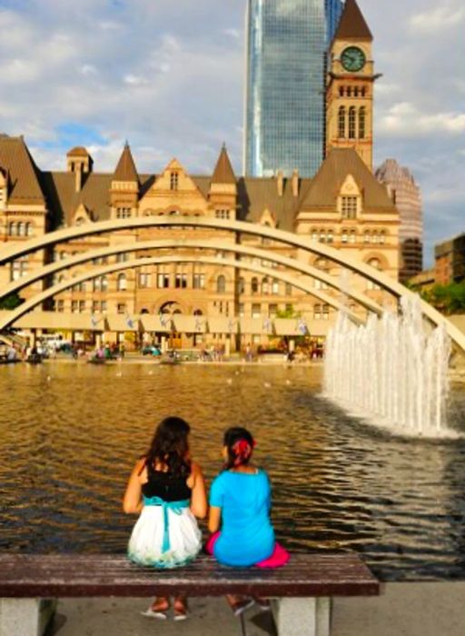 A pair of individuals relaxing on a bench by the waterfront in Toronto, with a fountain visible on the right.