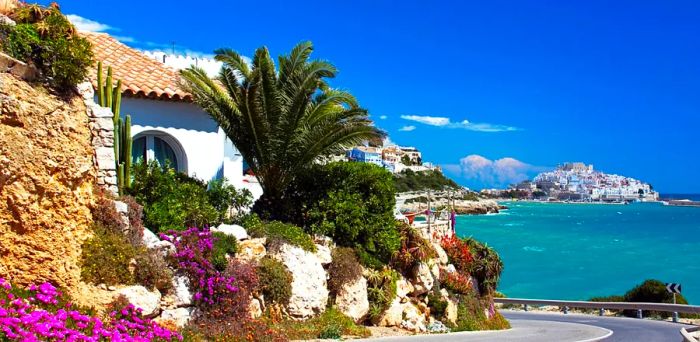 A white house along a winding road beside turquoise waters