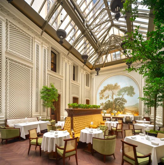 Saison restaurant features sunny yellow banquettes, crisp white tablecloths, a striking mural of trees, and a greenhouse-style ceiling.