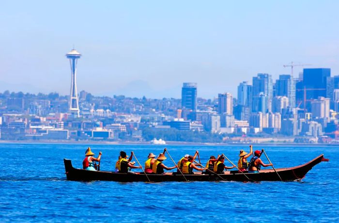 A group of Coast Salish individuals navigate a canoe through Seattle harbor.