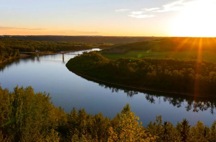 Sunset rays illuminate the North Saskatchewan River and the Terwillegar Park Footbridge in Edmonton, Alberta.