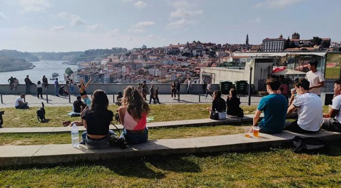 A scenic view of the waterfront in Porto, Portugal, from a terraced park where people are sitting and enjoying activities on the steps and grass.