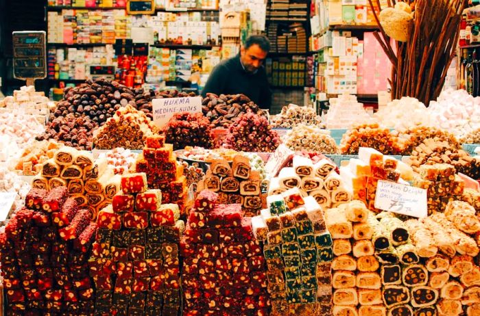 A vibrant display of colorful Turkish sweets with a shopkeeper in the background