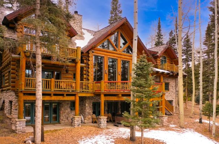 A log cabin-style mansion nestled among towering pine trees in Telluride, with patches of snow blanketing the ground.