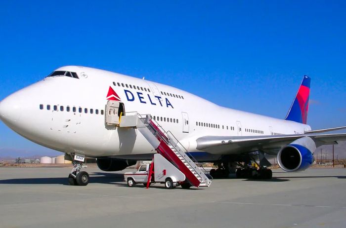 A white Delta Boeing 747 stationed at the airport, complete with a mobile stairway.