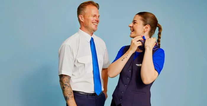 Two flight attendants from Scandinavian Airlines sporting short-sleeve uniforms, showcasing tattoos on their arms.