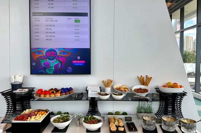 Brightline Premium lounge featuring a buffet of food and a train schedule overhead