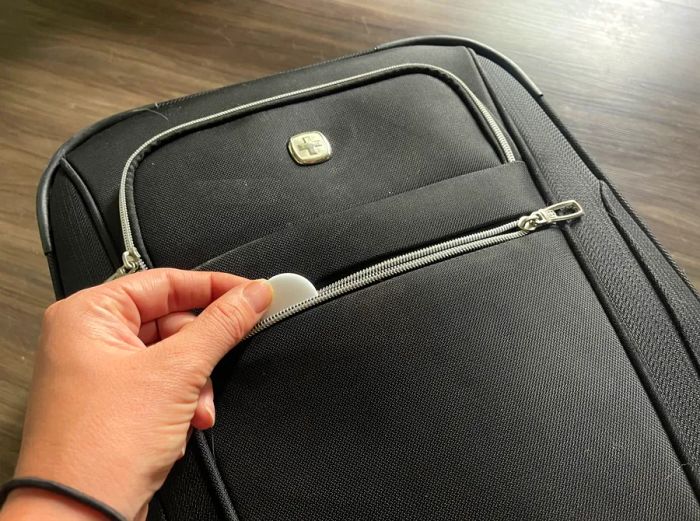 An Apple AirTag nestled in the pocket of a gray suitcase