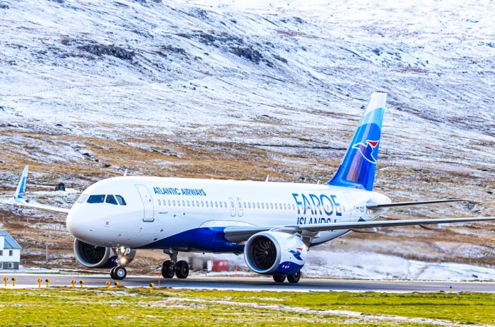 A white and blue Atlantic Airways Airbus A320neo is seen on the tarmac against a snowy backdrop.