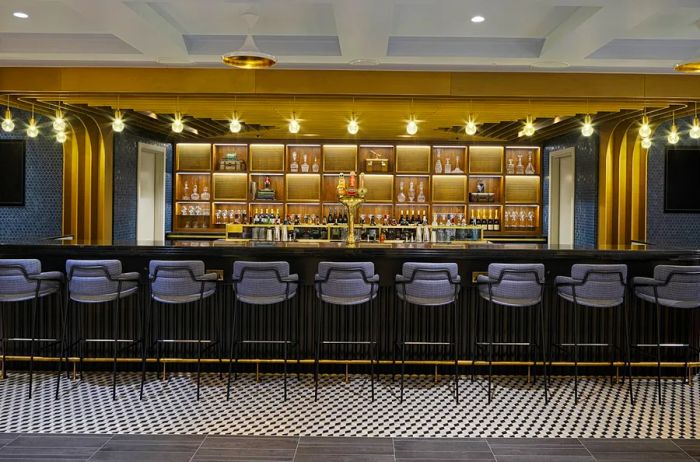 A stylish bar featuring gold and gray tones in the London Heathrow lounge, with a row of unoccupied seats.