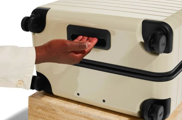 A hand gripping the handle on the base of a white suitcase