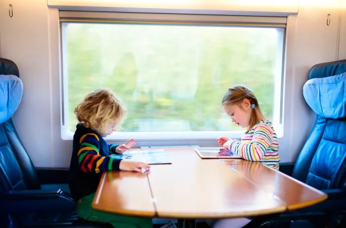 two children seated across from each other at a table on a train