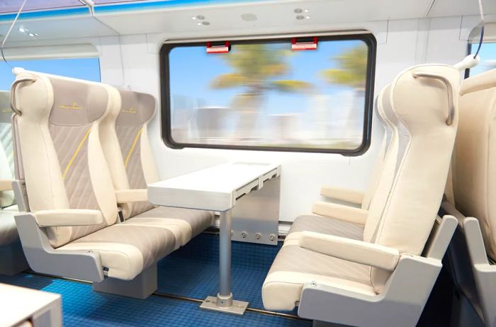 A set of four white Brightline train seats arranged to face each other with a table in the center.