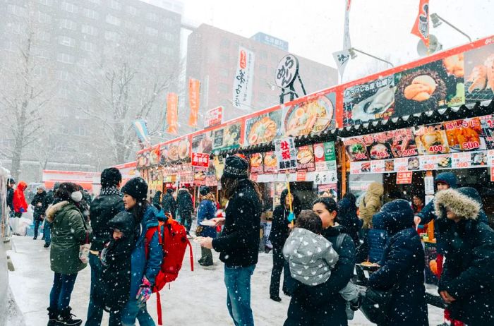 Individuals strolling past Japanese food stalls blanketed in snow