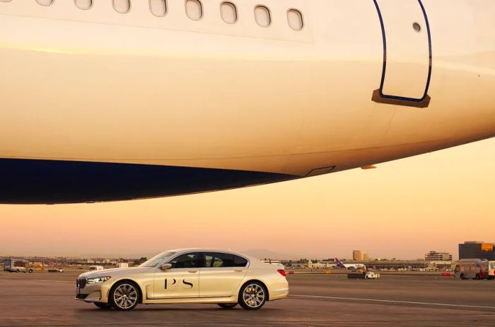 A white BMW with the PS logo driving beneath an aircraft on the tarmac