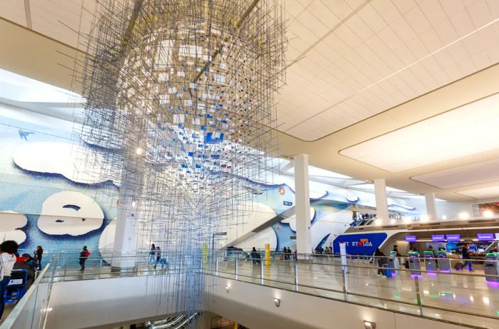 A striking modern art installation hangs in the central lobby of LaGuardia Airport, with check-in counters visible in the background.