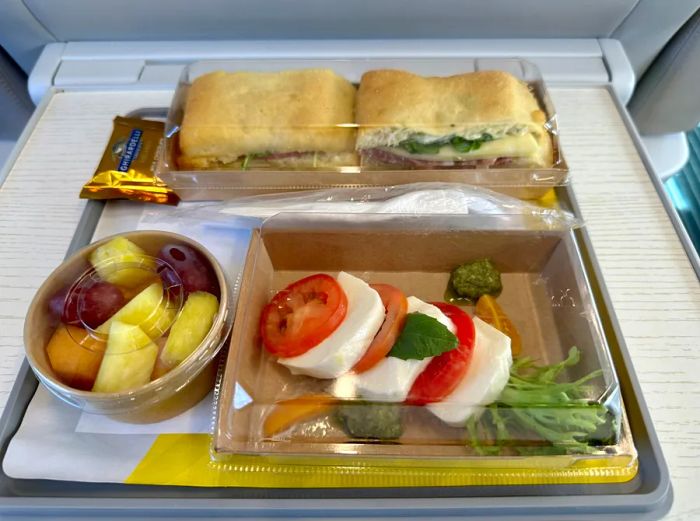 Fruit cup, burrata salad, and sandwich served on a tray