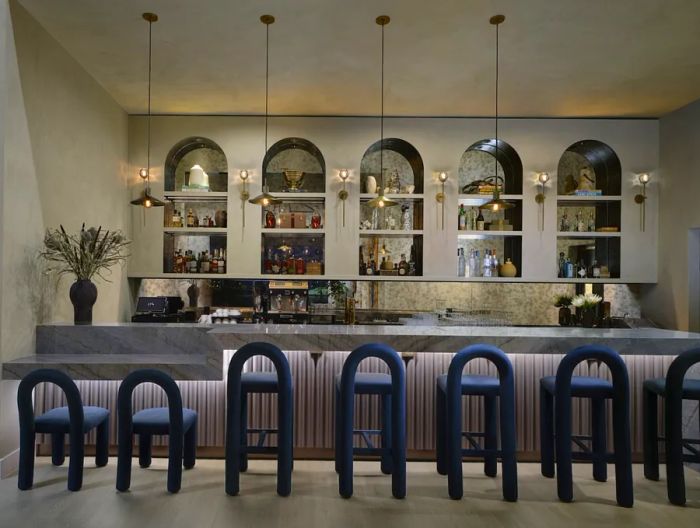 A row of unoccupied arched blue velvet chairs and barstools adorns the bar at PS Atlanta.