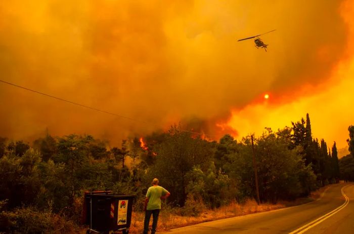 On August 18, 2021, a man observes a helicopter battling a fire in the village of Villa, located in Northwestern Athens.