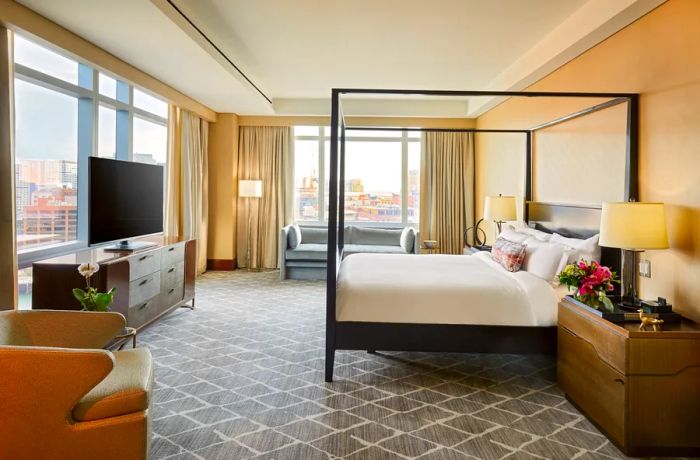 This guest room at the InterContinental Boston features an elegant four-poster bed and a large flat-screen TV set against a backdrop of gray carpeting.