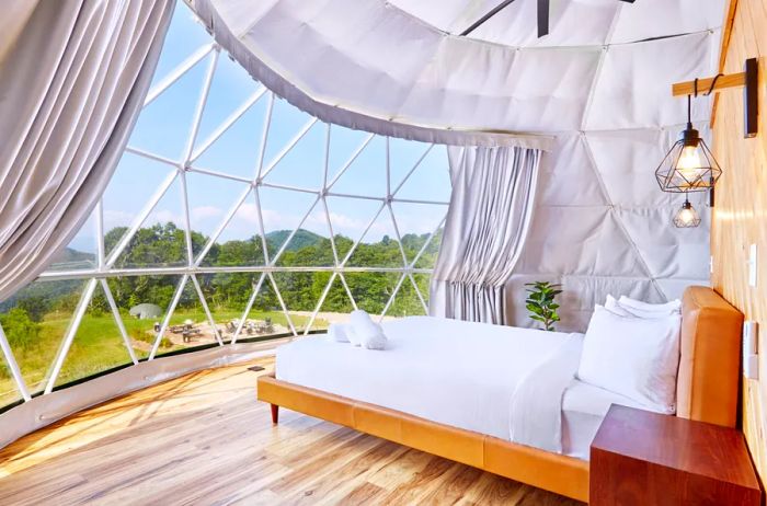 White bed positioned by a window with a view of the forest