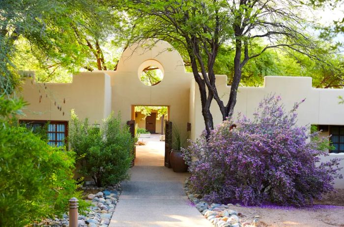 The exterior of Miraval Arizona, featuring white adobe walls nestled among lush trees and a large lavender bush.