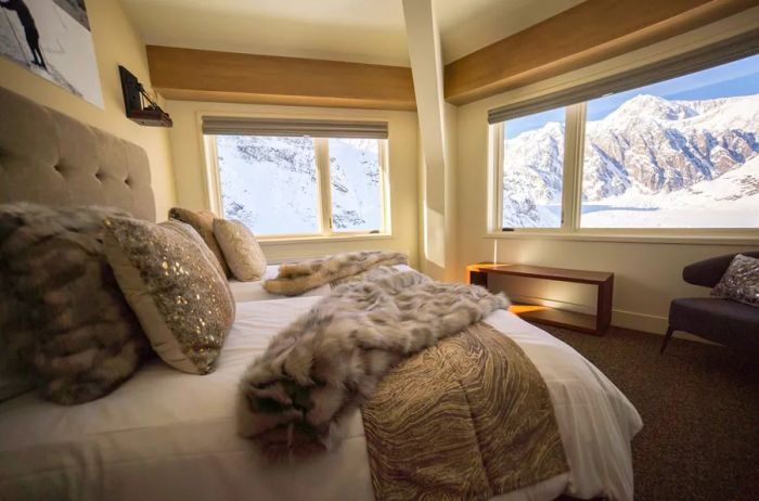 This guest room at Sheldon Chalet boasts a bed adorned with a faux fur throw and expansive windows overlooking the stunning landscape.