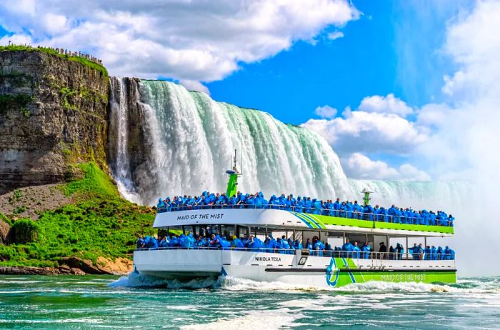 A boat filled with people in blue ponchos next to a waterfall