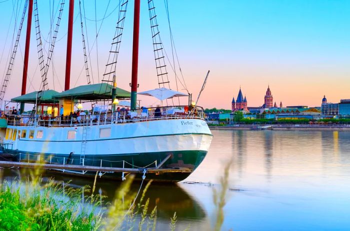 A picturesque view of people aboard a large sailboat gazing at Saint Martin's Cathedral in Mainz, Germany, across the Rhine River.