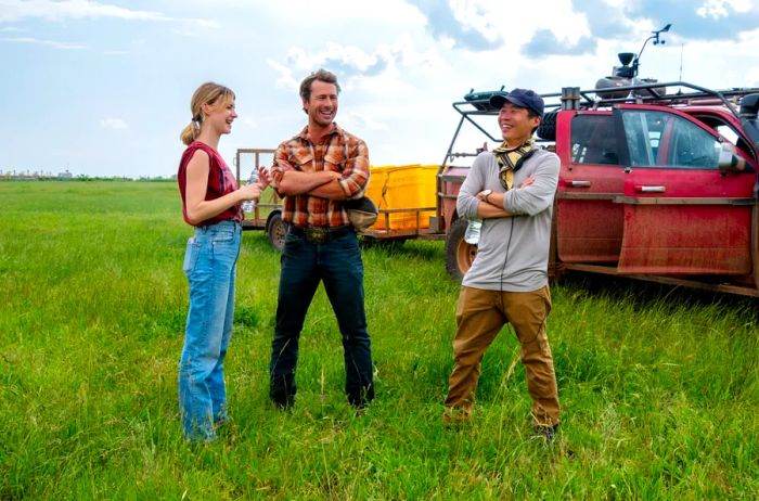 Daisy Edgar-Jones, Glen Powell, and Lee Isaac Chung pose in a field during the filming of Twisters.