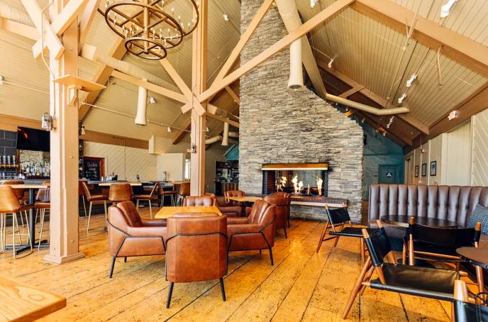 The bar area at Outbound Mammoth features a variety of brown armchairs, bar tables, and stools, centered around a large fireplace.