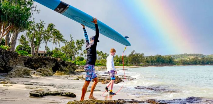 Two individuals heading into the Pacific Ocean with a surfboard.