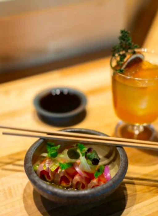 A plate of crudo accompanied by chopsticks and a cocktail at Handies Douzo.