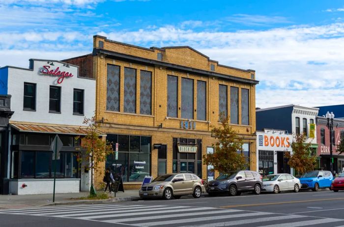 The exterior of the Black Cat, nestled among other small businesses in a bustling stretch of the Shaw-U Street neighborhood, with a line of cars parked out front.