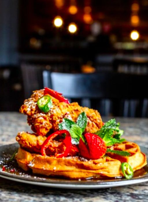 A side view of a plate featuring chicken and waffles at Lucille's, garnished with red and green elements.