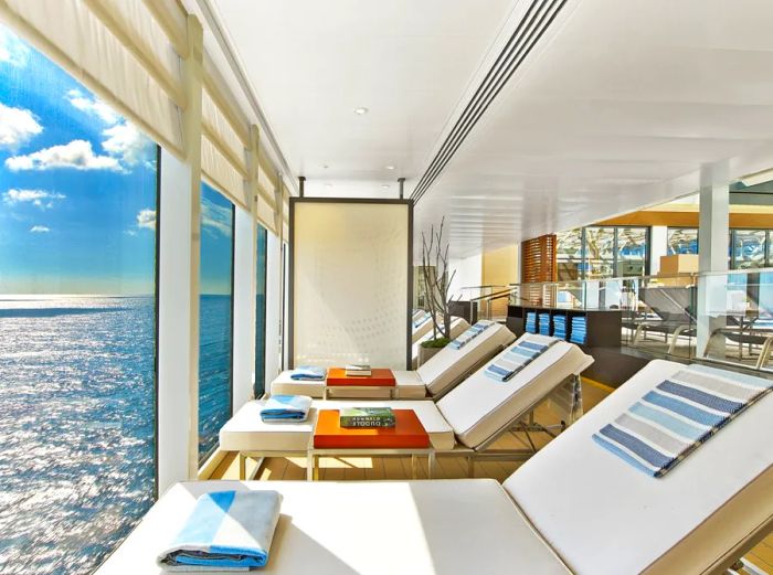 Rows of empty beige lounge chairs arranged along a wall of windows aboard a Viking ocean cruise ship