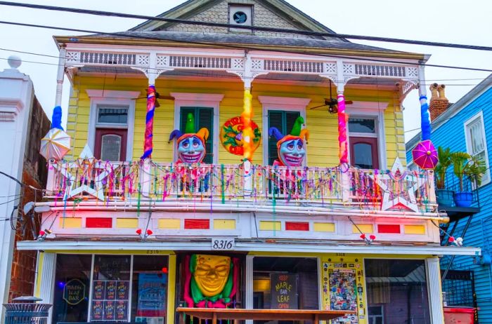 A vibrant yellow house adorned for Mardi Gras, showcasing two stories of porches