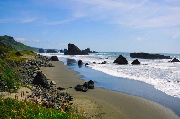 Waves gently retreating from a beach adorned with green grass and dark rocks along the shore.