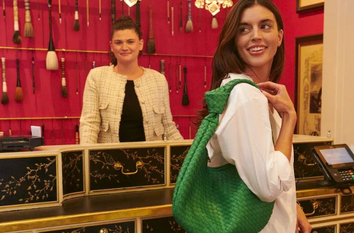 Hotel guest showcasing a green shoulder bag while interacting with the Kimpton hotel lobby clerk