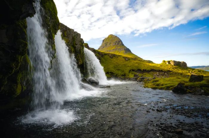 Kirkjufell Mountain stands majestically in the background with waterfalls cascading in the foreground near the Icelandic port town of Grundarfjörður