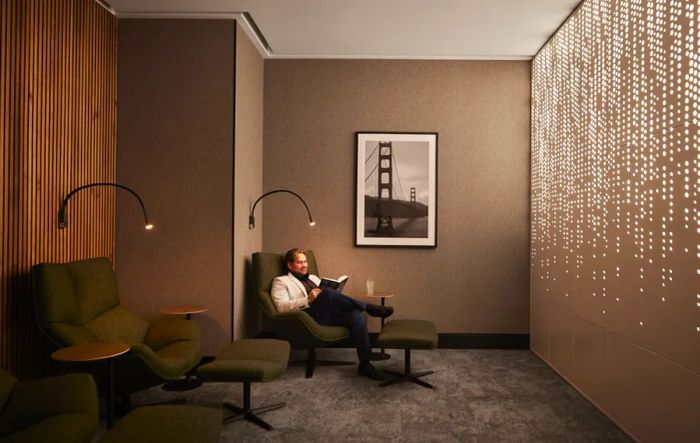 man relaxing in a green business lounge chair within a stylish gray room, featuring a light installation on the wall and a photo of the Golden Gate Bridge at the airport lounge Club SFO