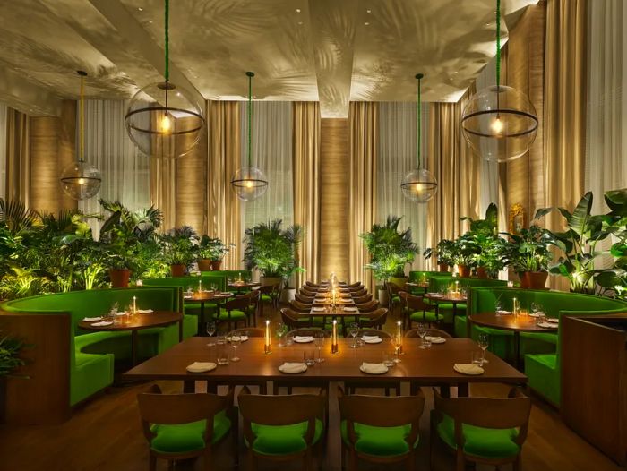 Lilac restaurant at the Tampa Edition hotel features U-shaped booths and long tables surrounded by green-upholstered chairs, all accented by tropical potted trees.