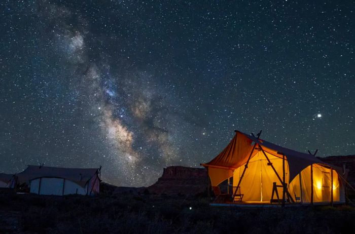 Experience tent accommodations at Under Canvas Moab, featuring lighting inside the tent and a clear view of the stars shining in the night sky above.