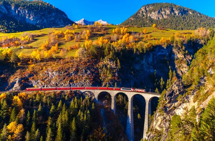 A red train traverses a high bridge, surrounded by the majestic mountains of Switzerland.