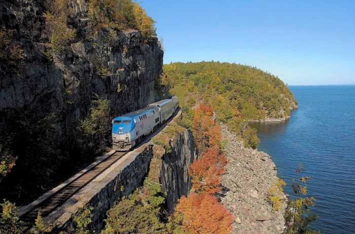 A blue Amtrak train travels alongside water in New York