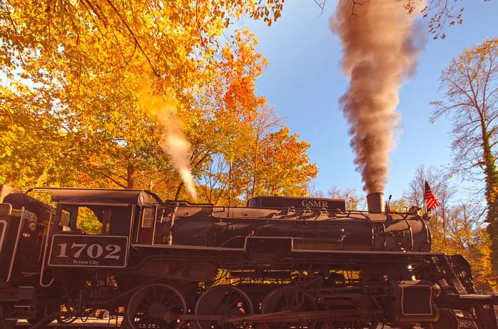 A vintage steam train engine travels through the colorful fall foliage of western North Carolina