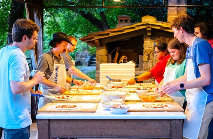 Group of young adults making pizzas in an outdoor kitchen